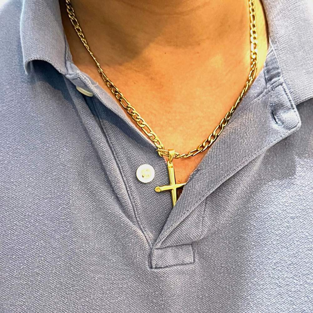 A close-up view of a person wearing a 24K gold-plated cross pendant necklace on a 14K gold-plated Figaro chain, styled over a light blue collared shirt